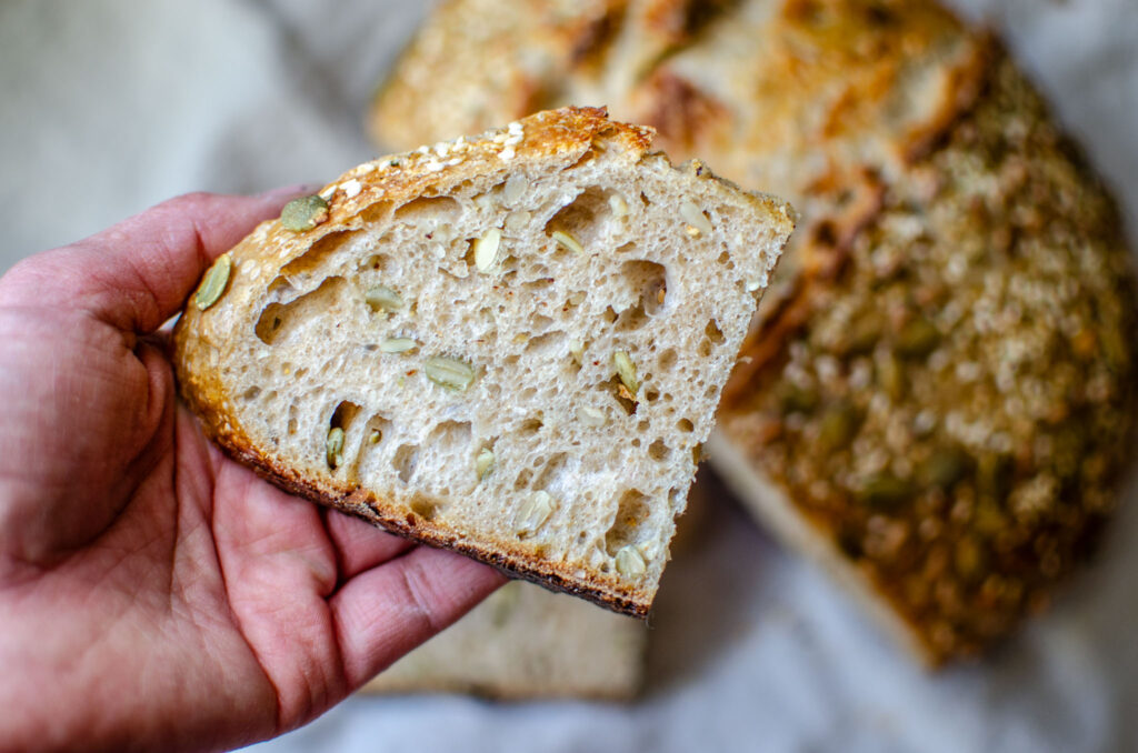 holding a piece of seeded multigrain sourdough bread above the loaf