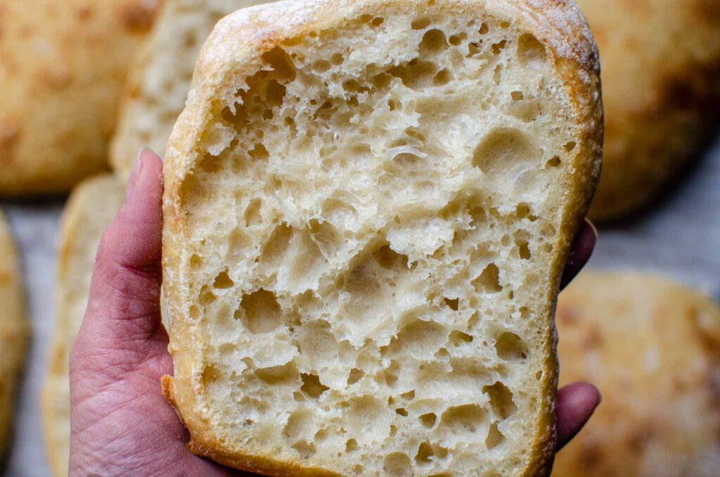 Holding a cut open sourdough ciabatta roll above other rolls