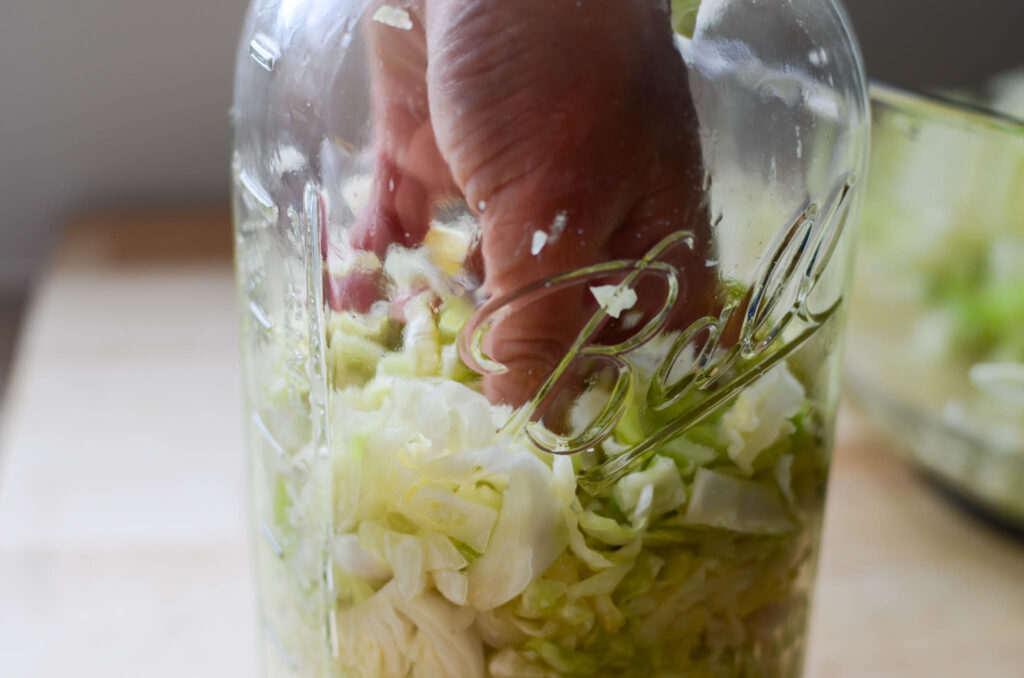 pressing Probiotic Rich Homemade Fermented Sauerkraut into a glass mason jar