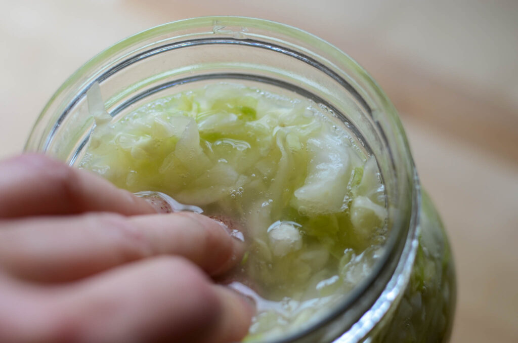 pressing Probiotic Rich Homemade Fermented Sauerkraut into a glass mason jar full