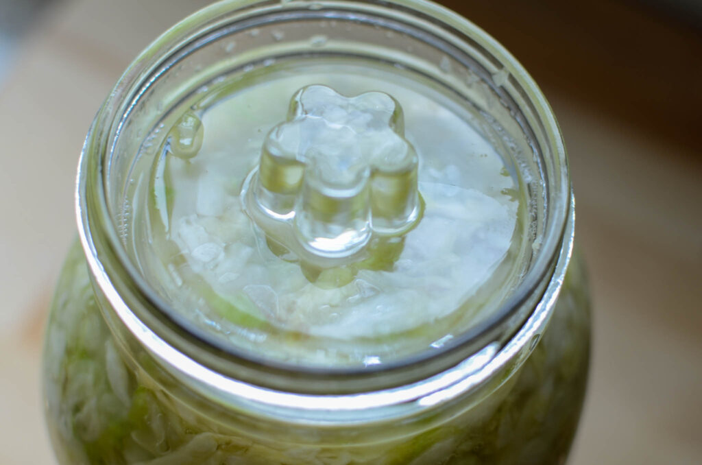 a glass jar of  Probiotic Rich Homemade Fermented Sauerkraut with a glass weight