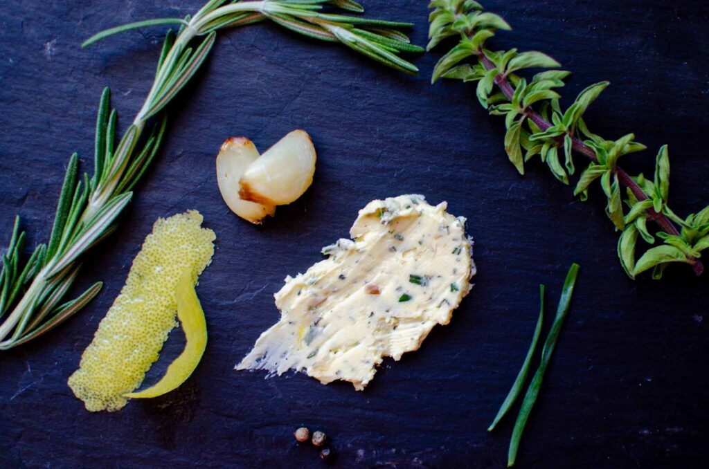 Black slate with roasted garlic cloves, herbs, lemon rind and a smear of garlic herb butter compound