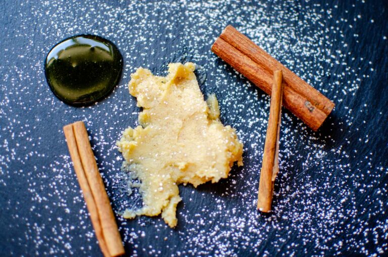 Whipped honey butter spread on black slate with powdered sugar sprinkled, a dollop of honey, and cinnamon sticks.