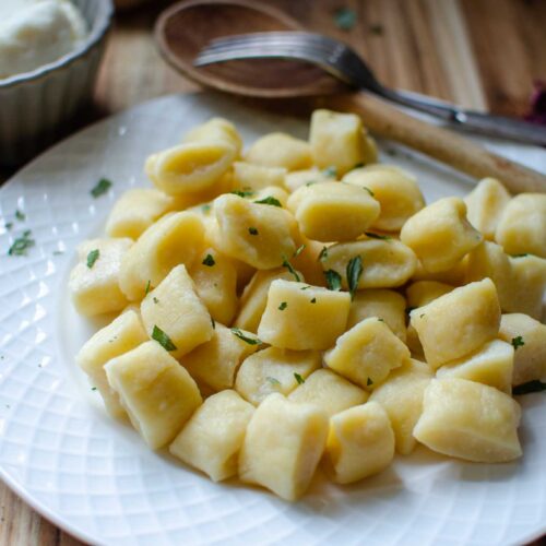 White plate full of ricotta gnocchi with dried basil sprinkled over