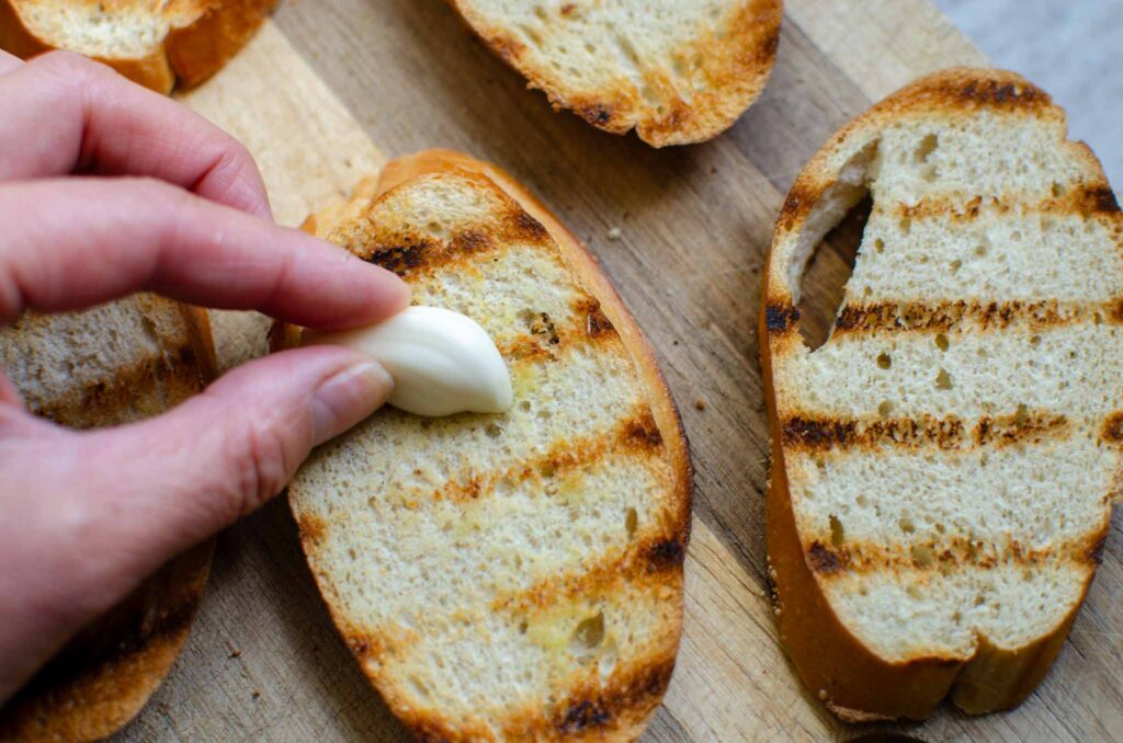 gently rubbing garlic clove on grilled bread 