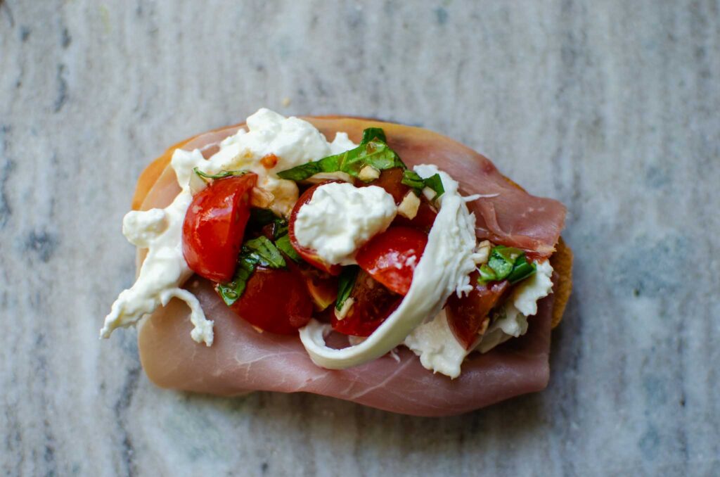 Adding tomato bruschetta on top of burrata and prosciutto toast.