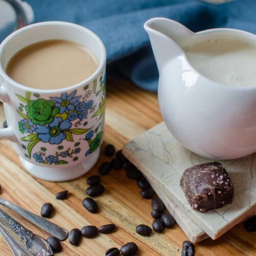 a cup of coffee with Homemade Italian Sweet Cream Coffee Creamer, coffee beans and pieces of chocolate candies