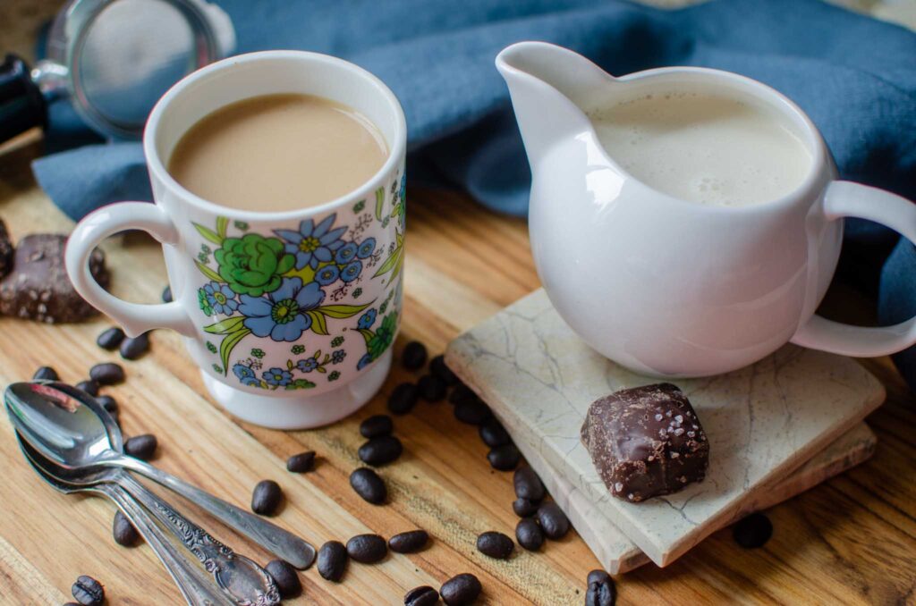 a cup of coffee with Homemade Italian Sweet Cream Coffee Creamer on wooden board with coffee beans and chocolate candies