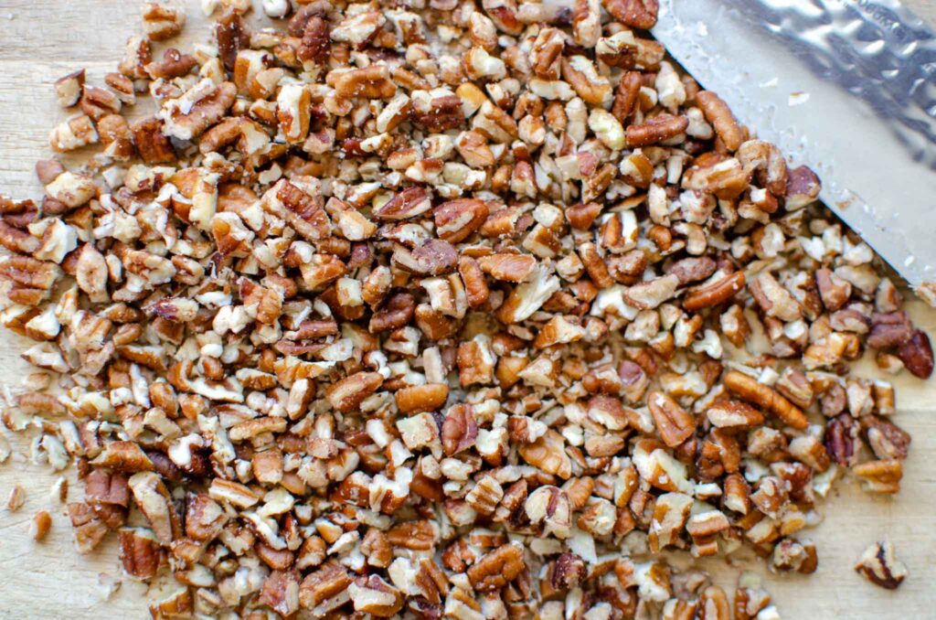 Chopped pecans on wood cutting board with knife