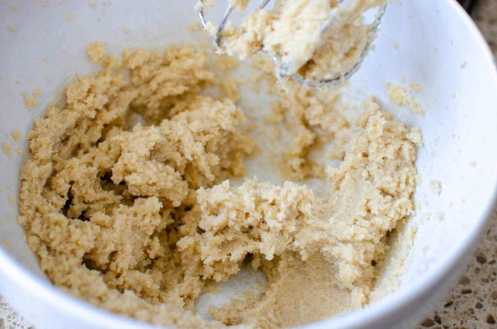 Creamed butter and sugar in white mixing bowl with hand mixer beaters