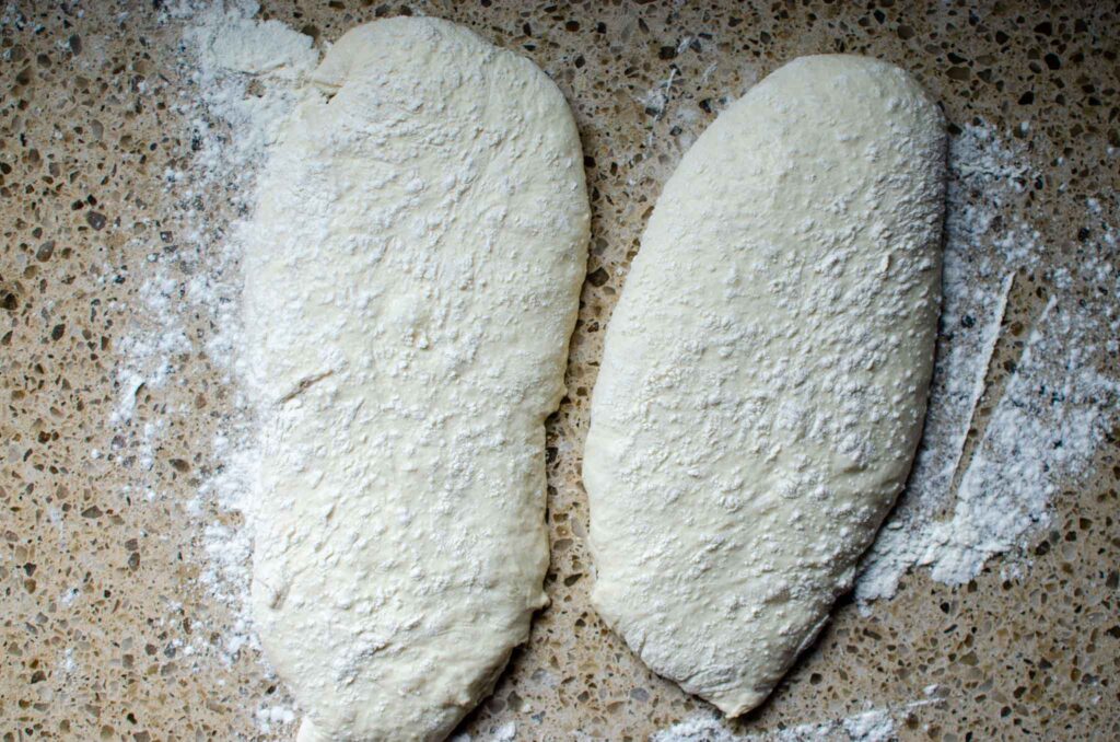 Sourdough ciabatta dough divided into two loaves on a floured work surface 