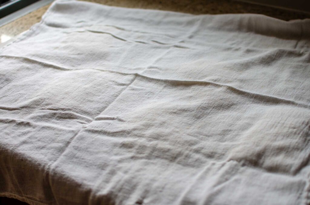 Sourdough ciabatta rolls on parchment paper during the final proof under a clean kitchen towel