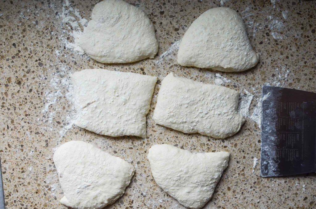 Sourdough ciabatta dough divided into rolls with a bench scraper on a floured work surface