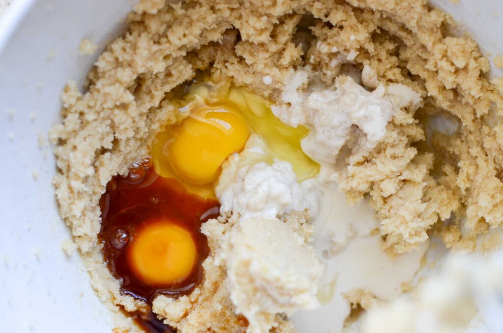 eggs, vanilla and sourdough discard in white mixing bowl with creamed butter and sugars