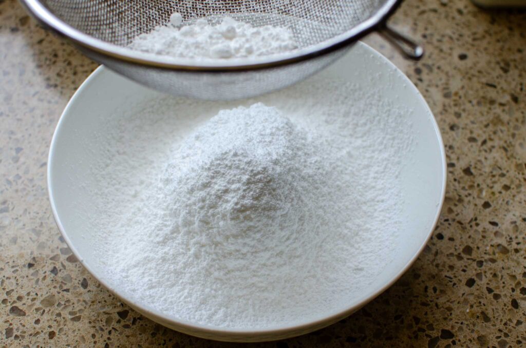 sifting powdered sugar into a white bowl