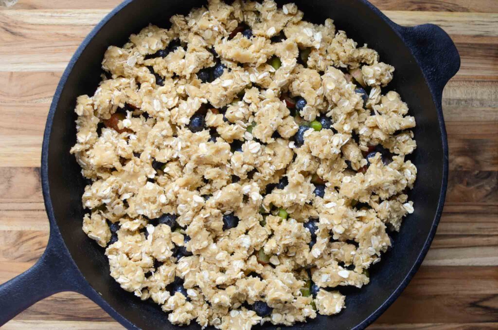 blueberry rhubarb crisp fruit mixture with oatmeal crisp topping in large cast iron skillet