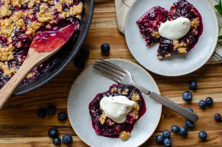 Two plates and a cast iron skillet with blueberry rhubarb crisp and whipped topping.