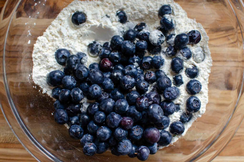 Dry ingredients with fresh blueberries in glass bowl for sourdough blueberry muffins