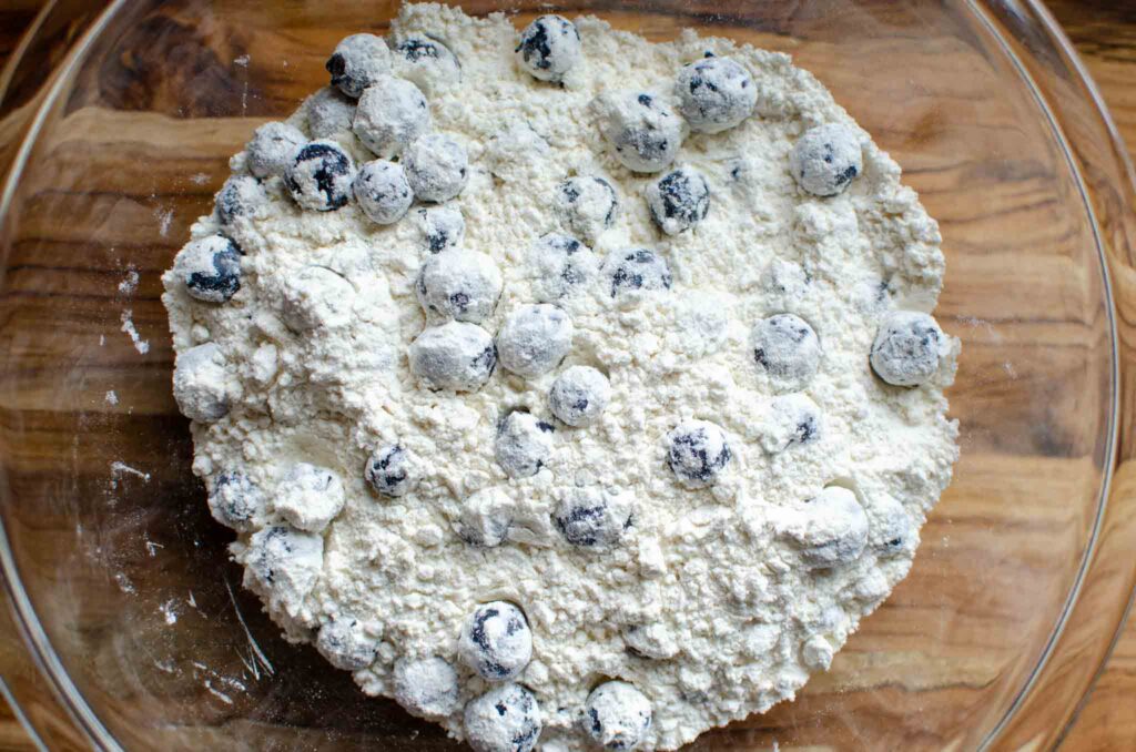 Dry ingredients tossed with fresh blueberries in glass bowl for sourdough blueberry muffins