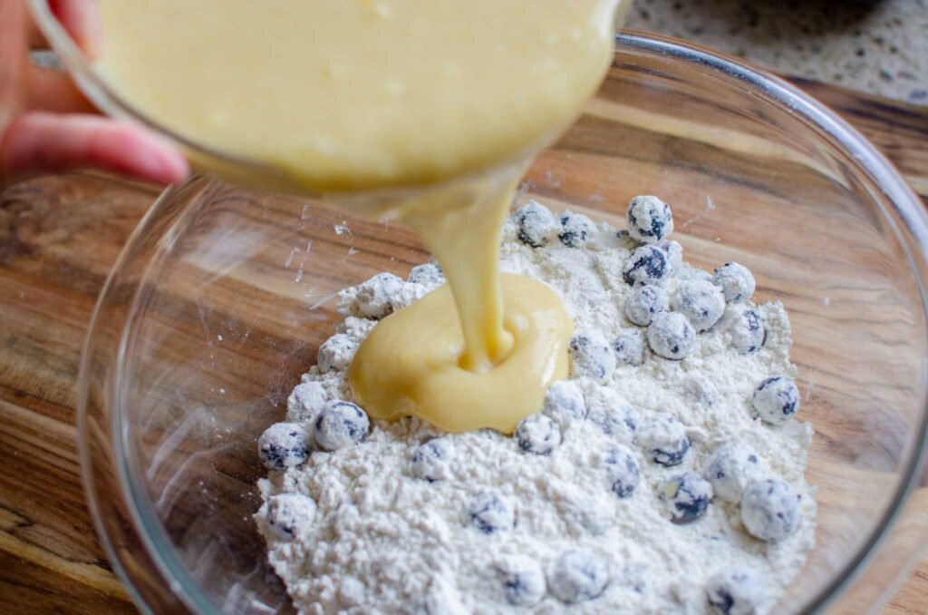 Pouring the wet ingredients for sourdough blueberry muffins into the dry ingredients.