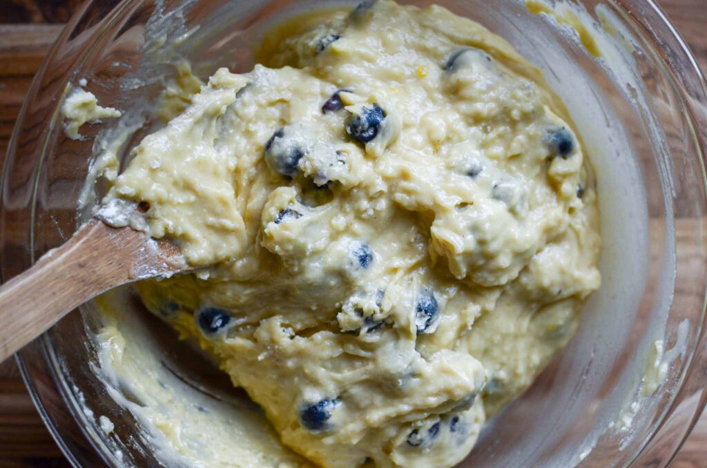 Sourdough blueberry muffin batter in a glass bowl and wooden spoon