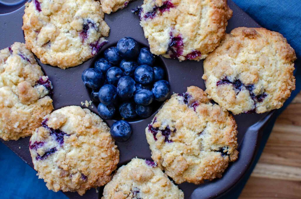 baked sourdough blueberry muffins in a muffin tin with one spot filled with fresh blueberries