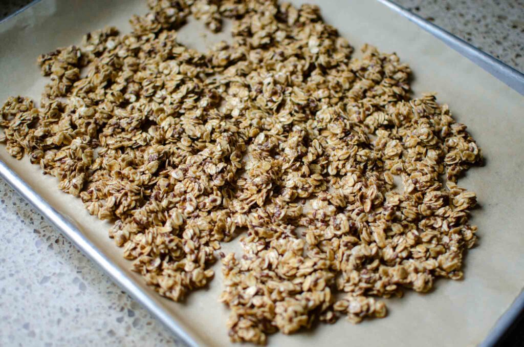 spreading sourdough granola on parchment lined baking sheet