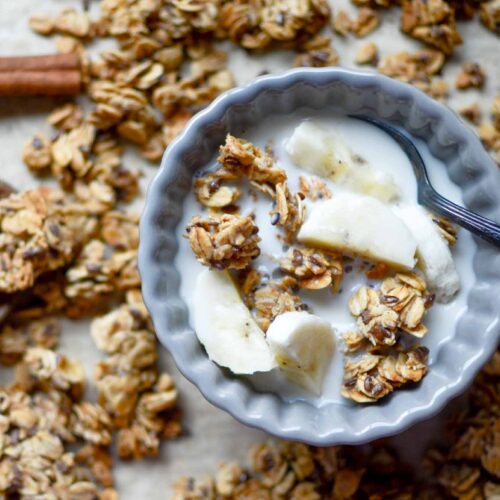 a small bowl of sourdough granola clusters and milk and sliced bananas with sourdough granola sprinkled all around