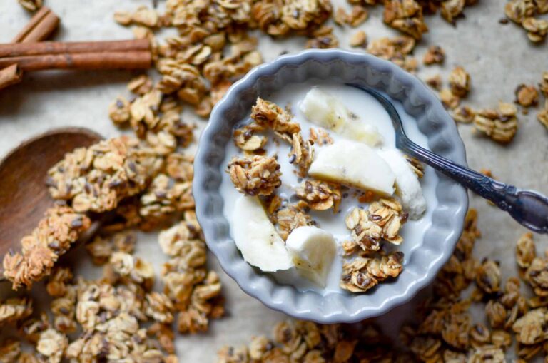 a small bowl of sourdough granola clusters and milk and sliced bananas with sourdough granola sprinkled all around