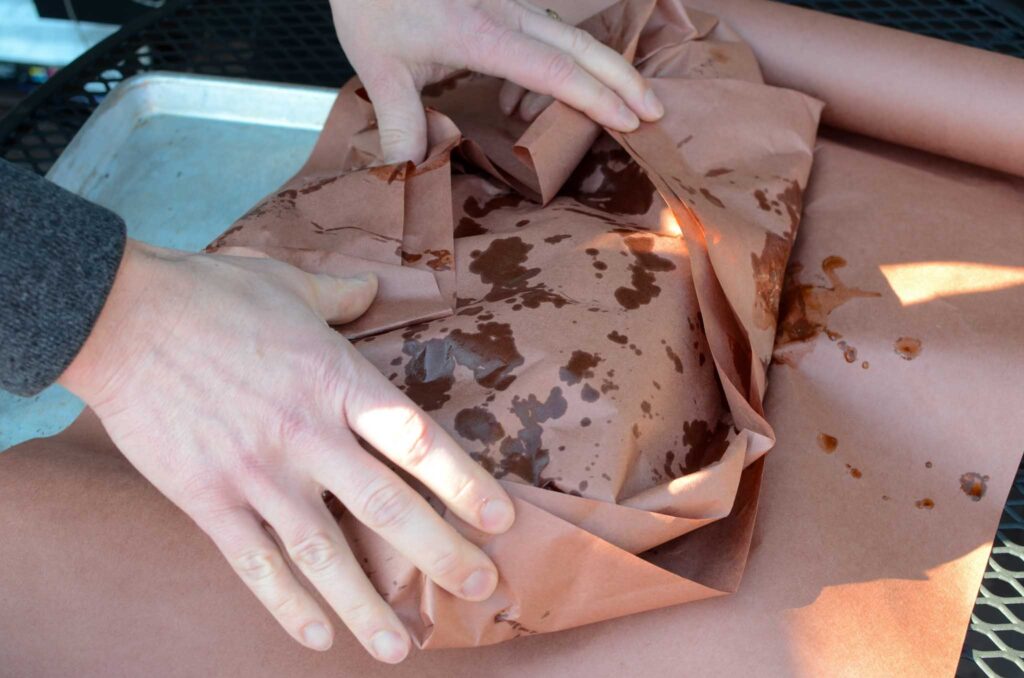 wrapping a smoked beef brisket in butcher paper to get through the stall