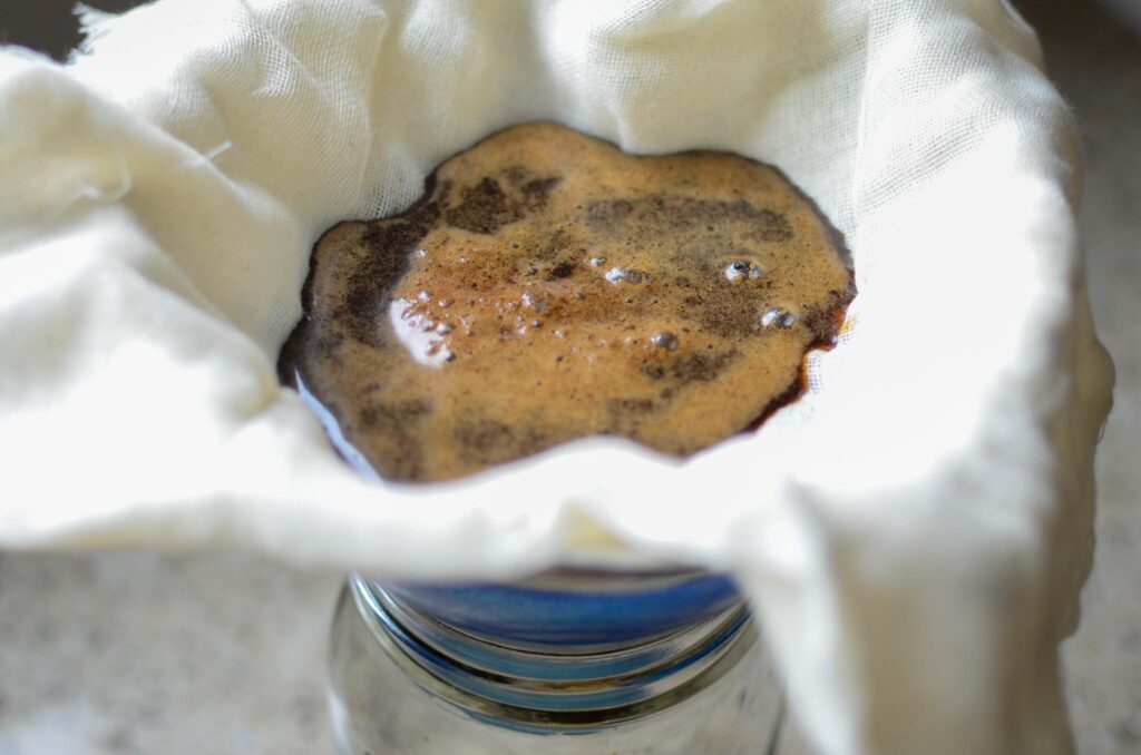 Cold brew coffee strained through cheese cloth over fine mesh strainer