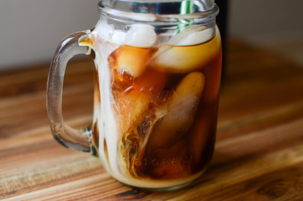 iced cold brew coffee with creamer in a glass mason jar and green striped straw