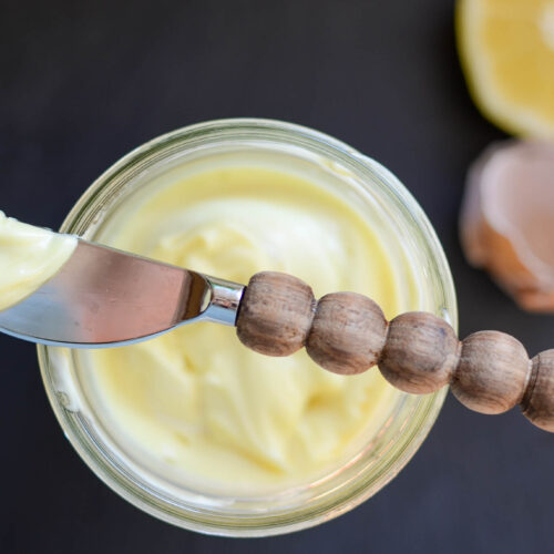 A mason jar of homemade mayo with spreading knife, egg shells and half of lemon