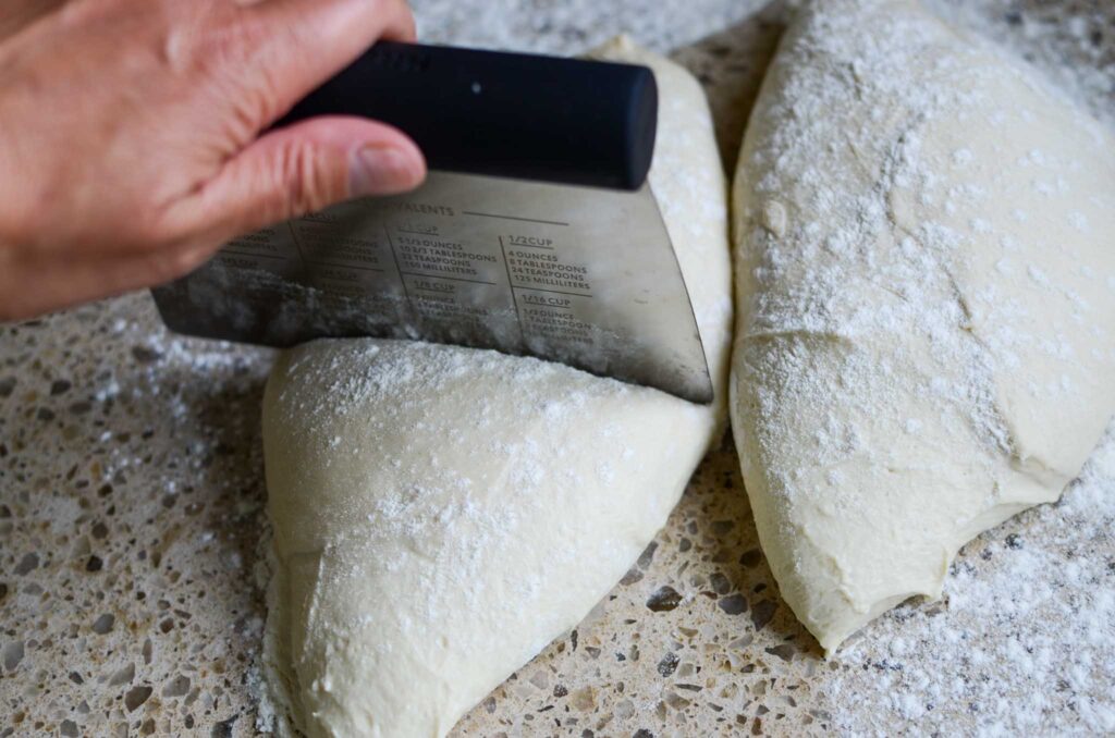 Sourdough pizza dough after bulk ferment on lightly dusted work surface being divided