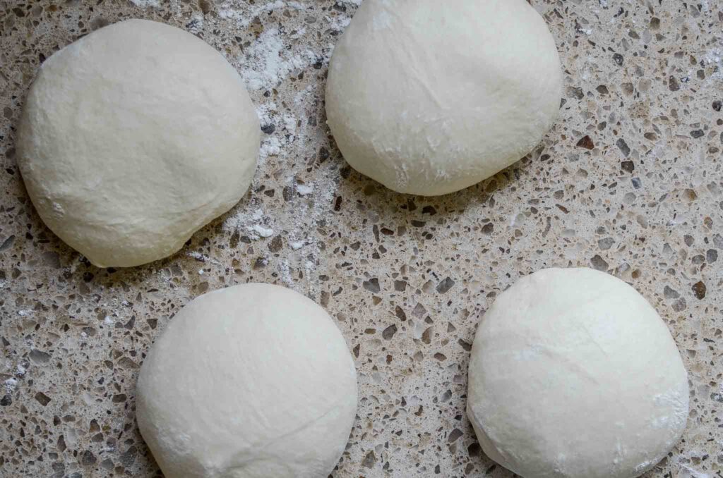 Sourdough pizza dough after bulk ferment on lightly dusted work surface being shaped into dough balls