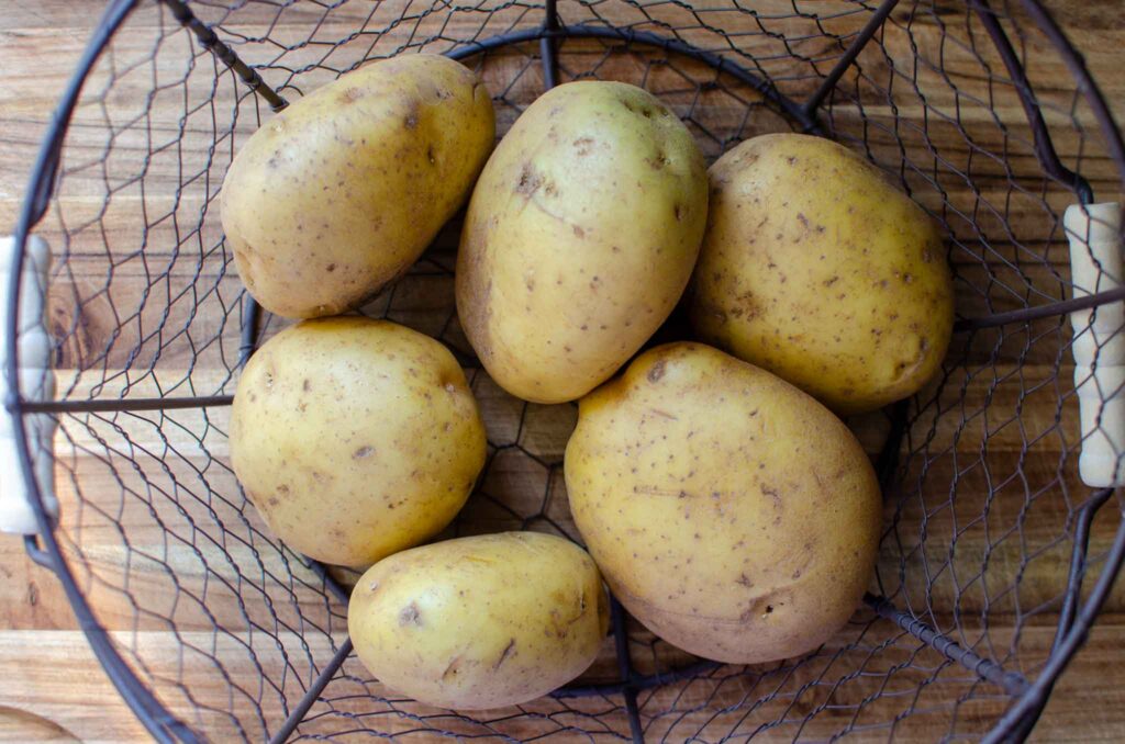 a wire basket filled with Yukon gold potatoes for a classic potato salad recipe