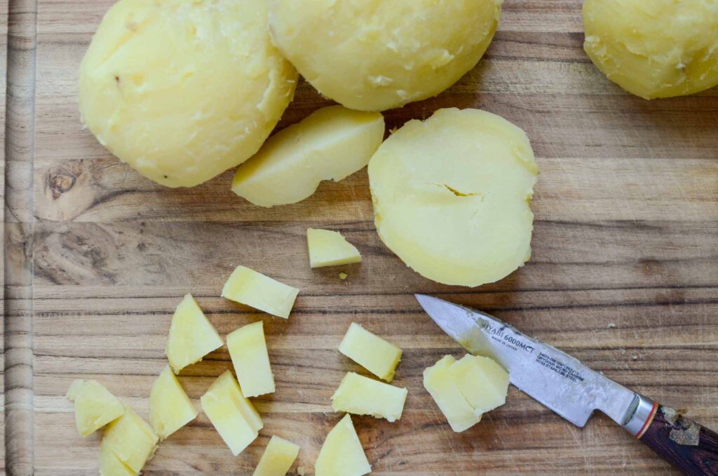 dicing Yukon gold potatoes with small knife on wooden cutting board to make classic potato salad