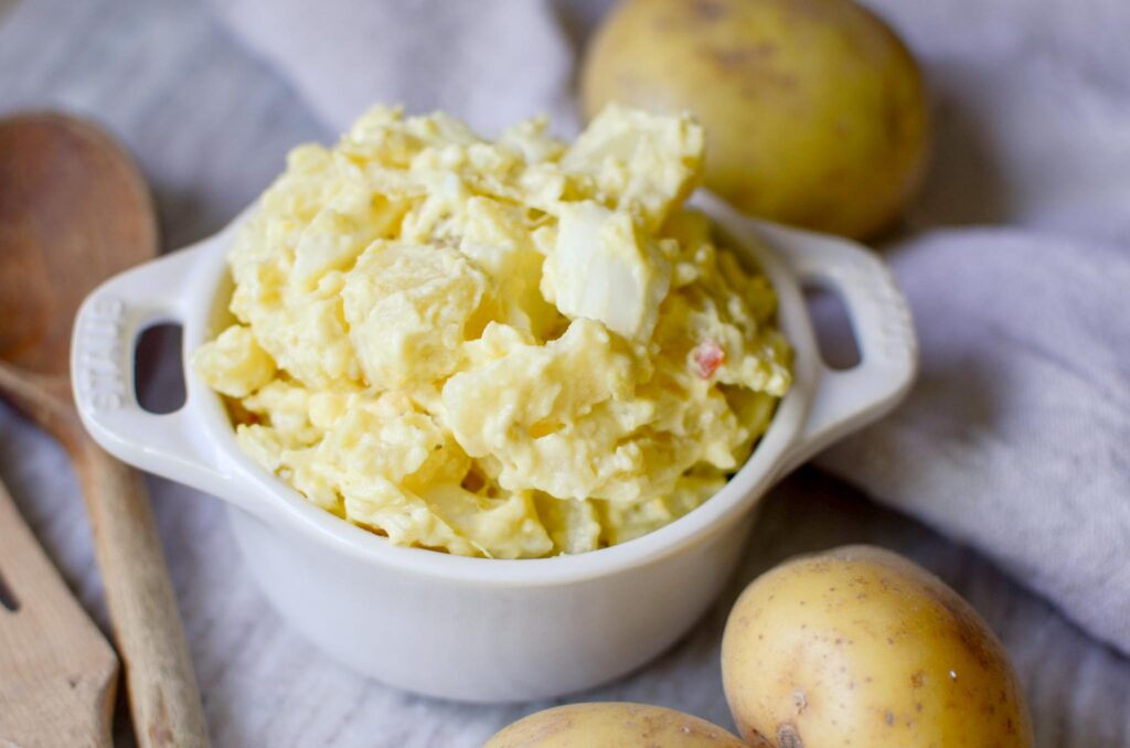 small staub baking dish filled with classic potato salad with potatoes next to dish. 