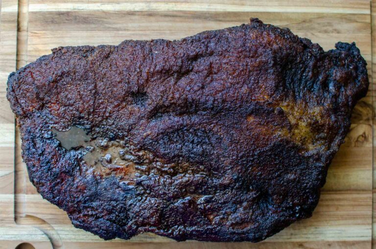 A whole smoked beef brisket on wooden cutting board