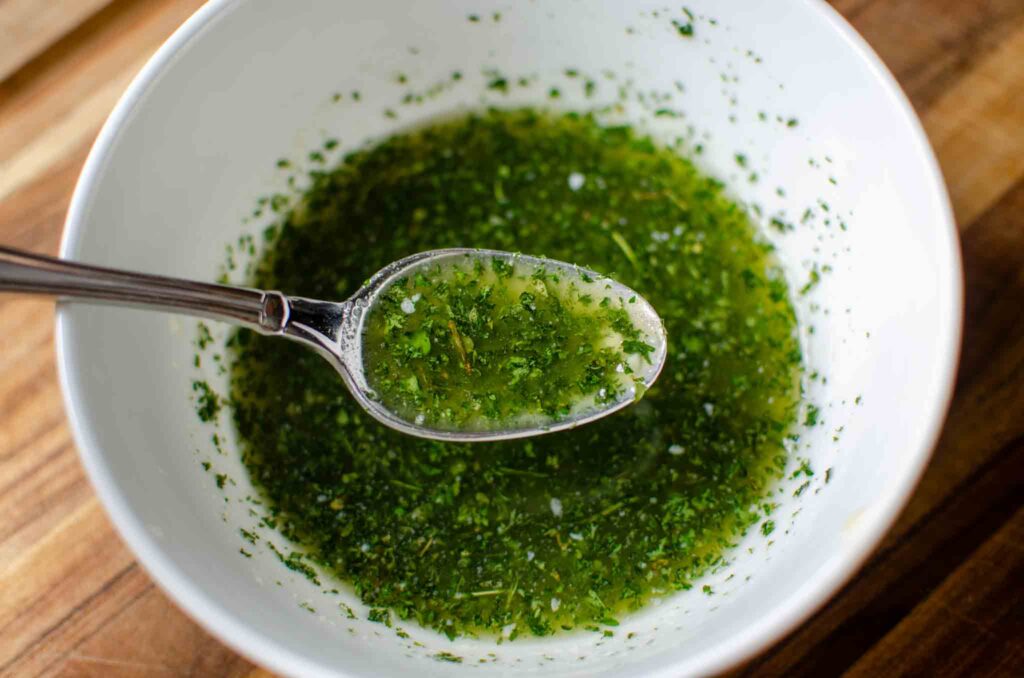 a white bowl of melted butter and herbs and garlic