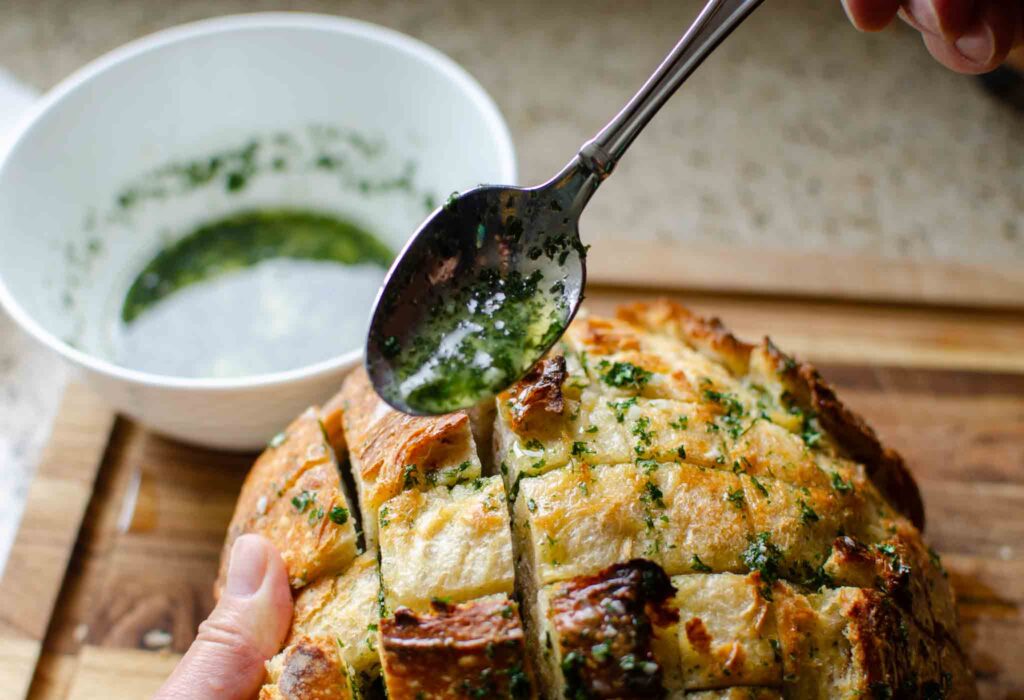 spooning the melted garlic and herb butter in Filling the Sourdough Cheese Bread