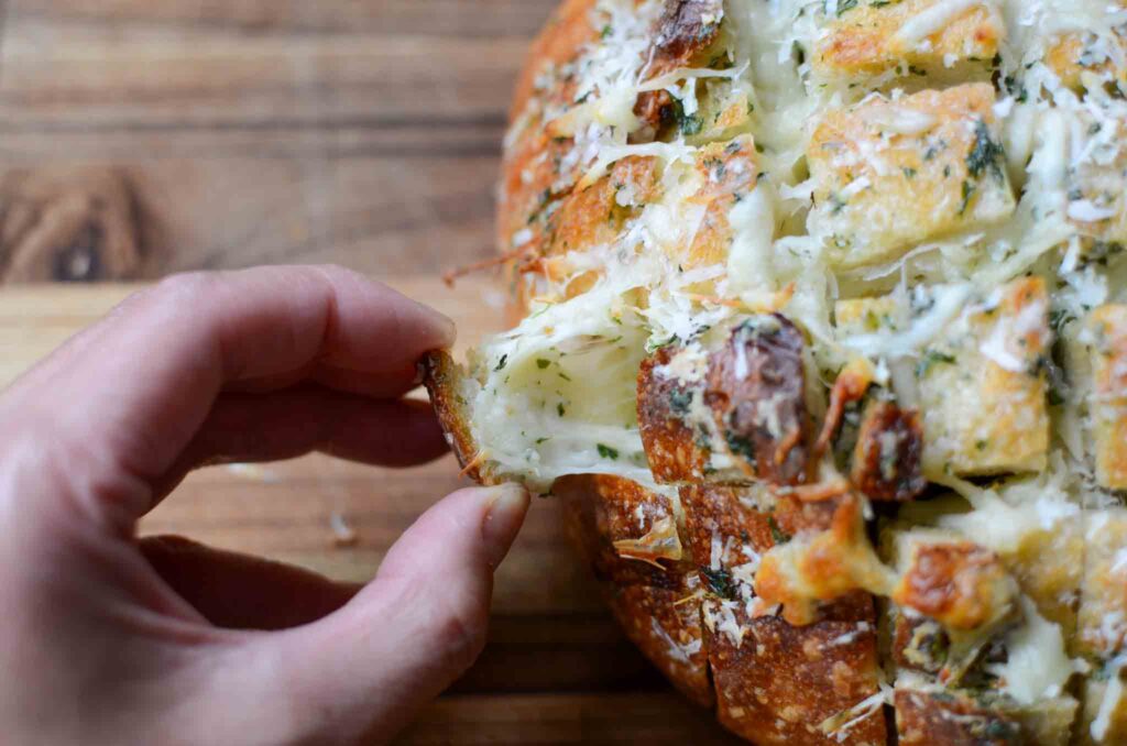 Pulling a piece off of a loaf of easy sourdough garlic and cheese pull apart bread