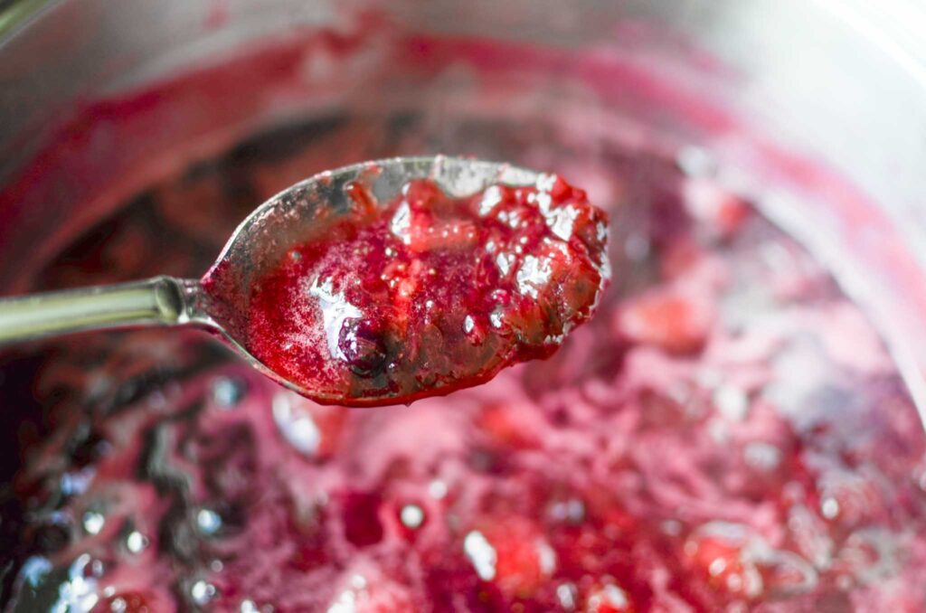 cooking mixed berry rhubarb jam with a spoonful of it