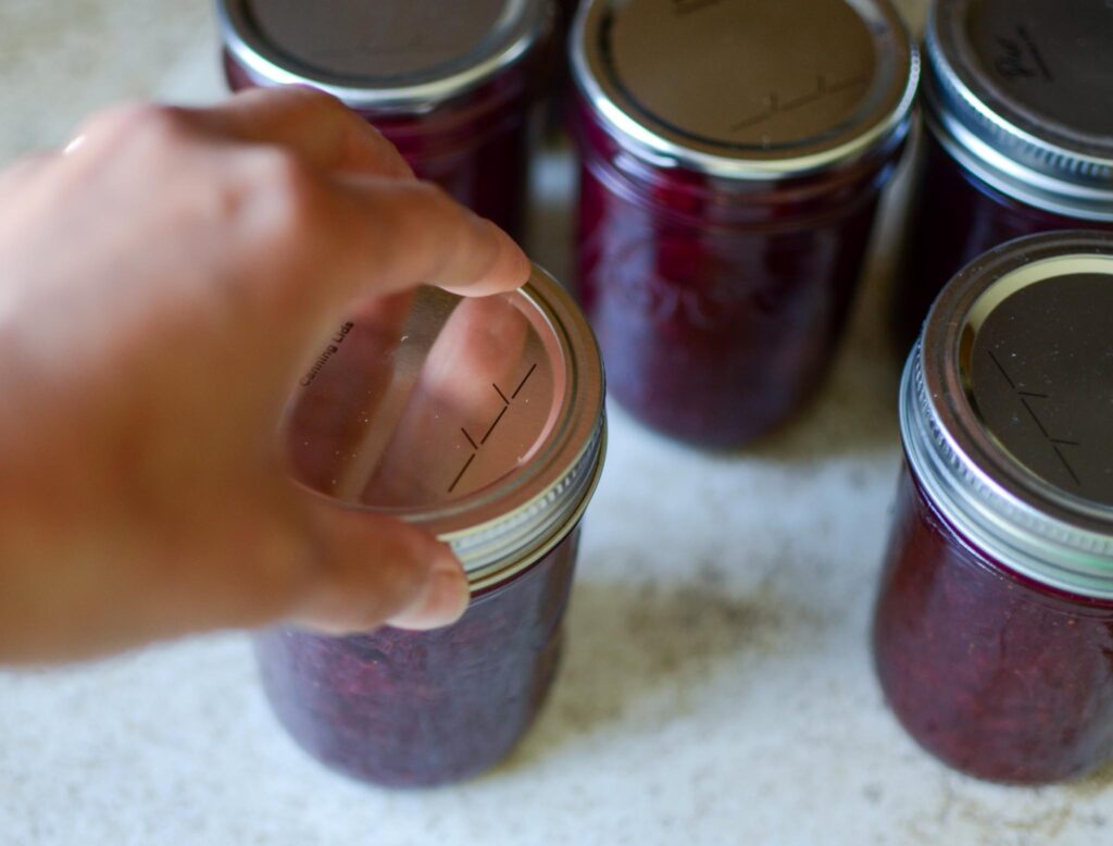 Twisting the two-piece canning lid onto jar of mixed berry rhubarb jam