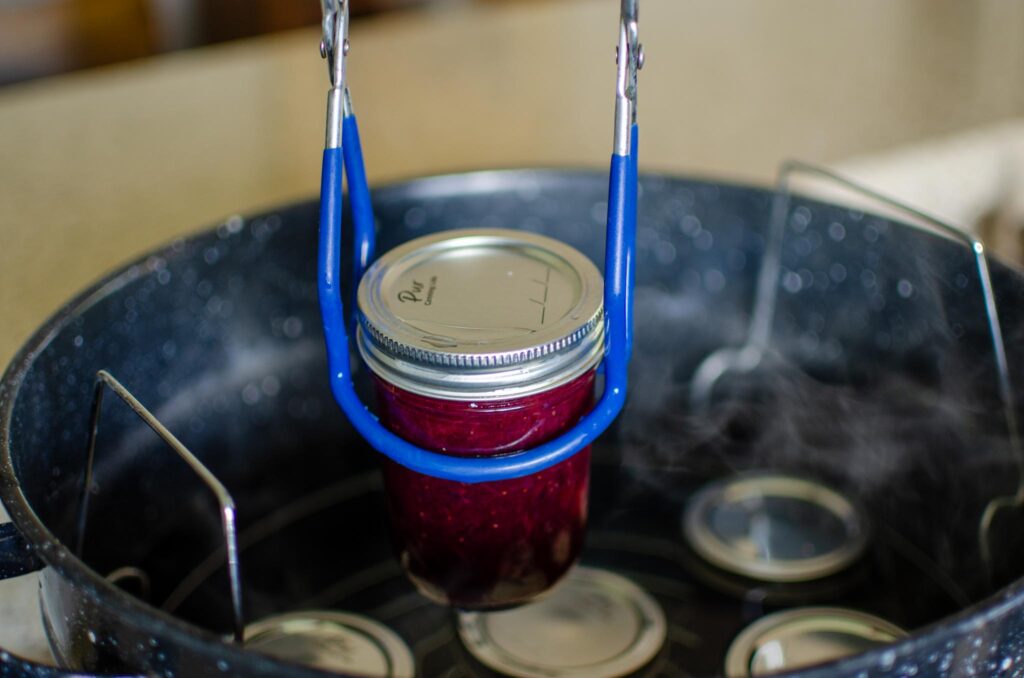 Lifting a jar of mixed berry rhubarb jam out of water bath canner using a jar lifter