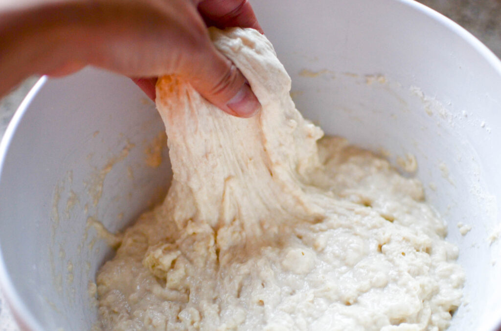 Sourdough cinnamon roll focaccia dough being stretched upward