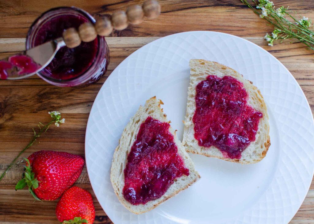 Two pieces of sourdough bread with mixed berry rhubarb jam on white plate