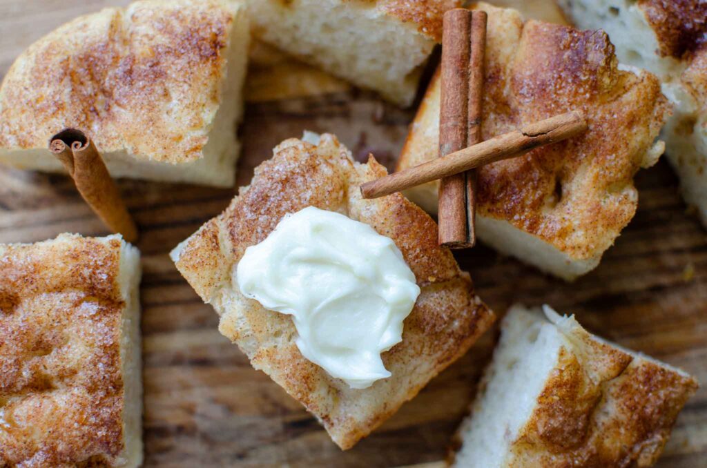 sourdough cinnamon roll focaccia pieces with cream cheese frosting and cinnamon sticks