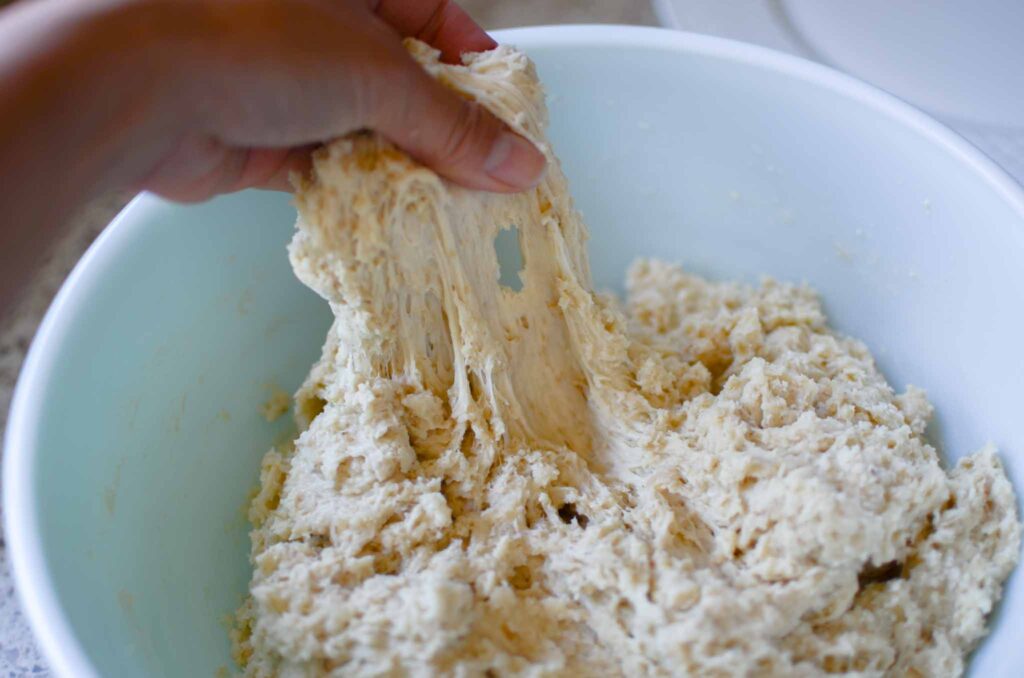 stretching the sourdough oatmeal dinner rolls dough in a large bowl