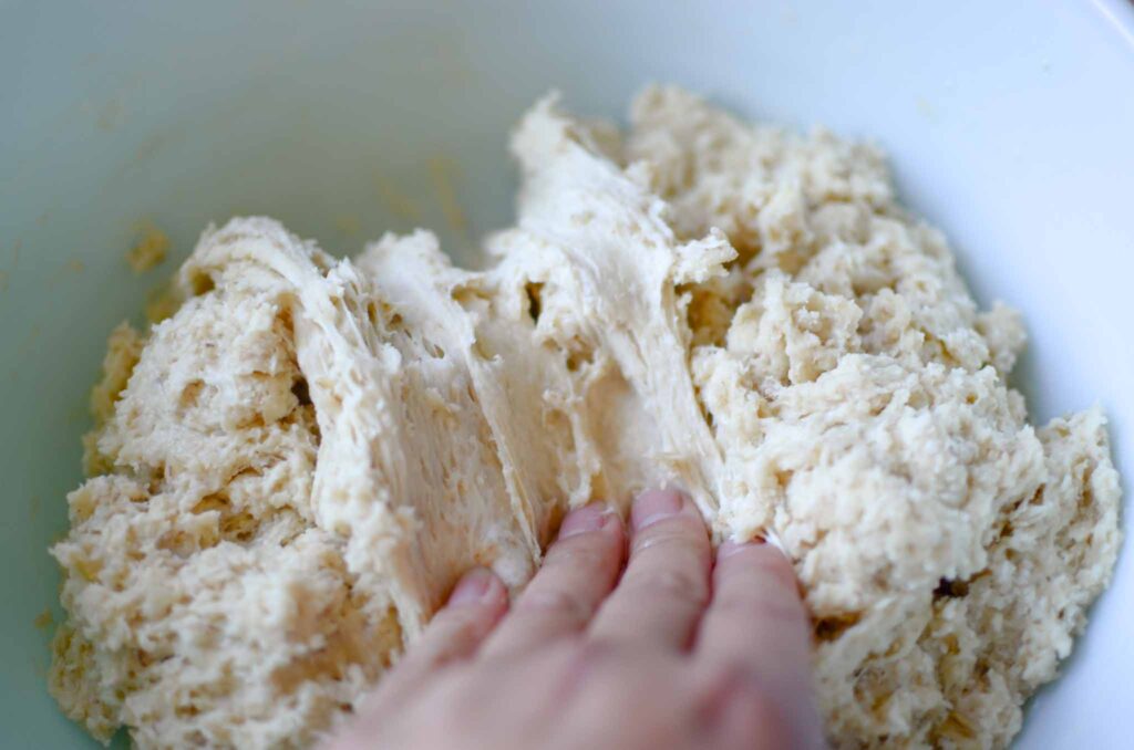 folding the sourdough oatmeal dinner rolls dough in a large bowl